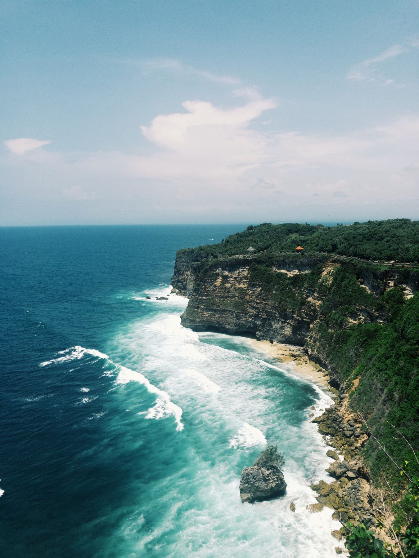 峇里島烏魯瓦圖情人崖，石灰岩峭壁沿海岸線延伸，崖下白浪一道道打上礁岩
